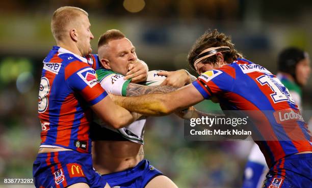 Blake Austin of the Raiders is tackled by Mitchell Barnett and Lachlan Fitzgibbon of the Knights during the round 25 NRL match between the Canberra...