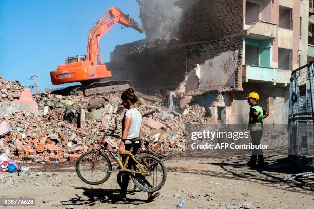 Woman carries a bike as a worker stands next to an excavator tearing down a building, during an urban rebuilding project, on August 25 in the Sur...