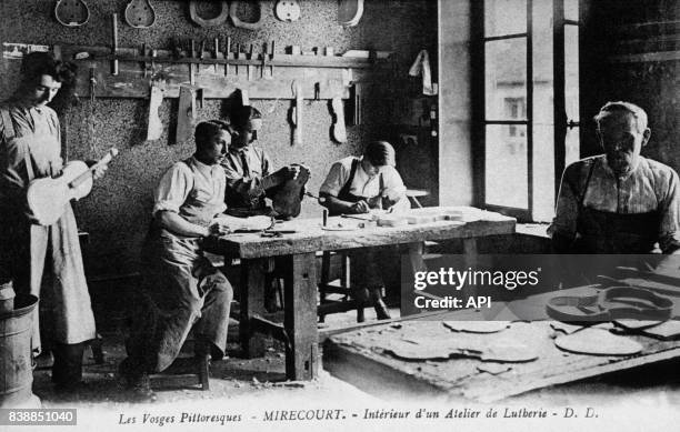 Carte postale illustrée par la photographie de l'intérieur d'un atelier de lutherie et ses artisans à Mirecourt, en France.