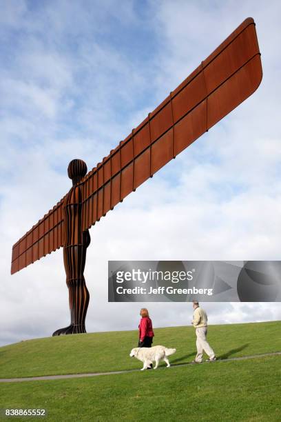 Couple walking there dog past the Angel of the North sculpture.