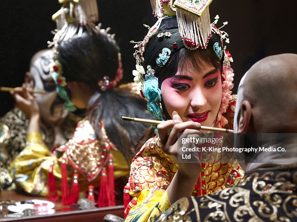 Chinese opera singer applying makeup to male