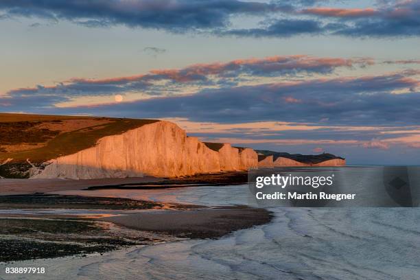 view to seven sisters chalk cliffs from cuckmere haven beach, sunset with moon. - seven sisters cliffs stock pictures, royalty-free photos & images