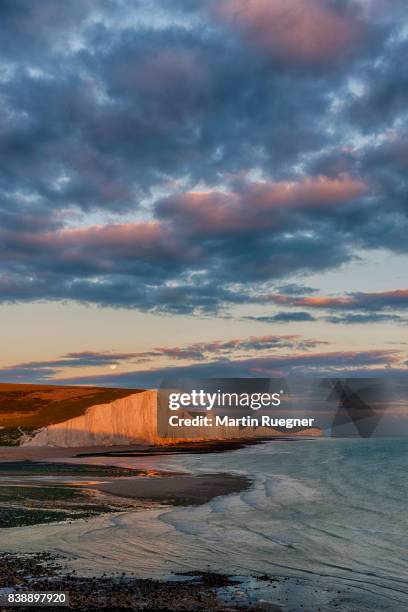 view to seven sisters chalk cliffs from cuckmere haven beach, sunset with moon. - seven sisters uk stock pictures, royalty-free photos & images