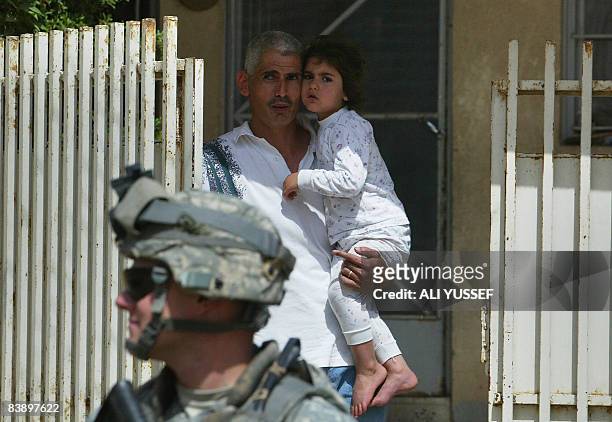 An Iraqi man holds his daughter as an US soldier from 3rd squadron 3rd armored cavalry is seen during a joint patrol with Iraqi soldiers of the 2nd...