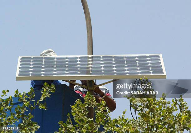Municipal worker adjusts a solar panel attached to the top of an electricity pylon along the central isle of a main road in the Karada district of...