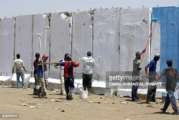 Iraqi men paint sections of a cement block wall, constructed jointly by the US and Iraqi army to prevent rocket attacks by Shiite militiamen, in the...