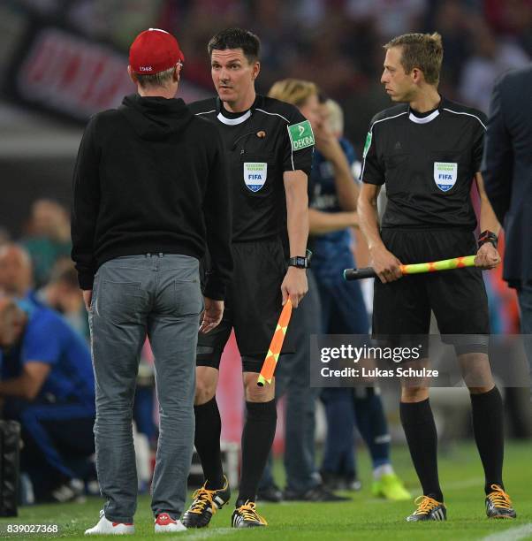 Peter Stoeger, coach of Koeln, speak with linesman mark Borsch and Stefan Lupp while the match is halted during the Bundesliga match between 1. FC...