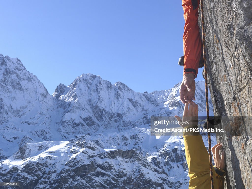 Climber helping teammate climb steep cliff