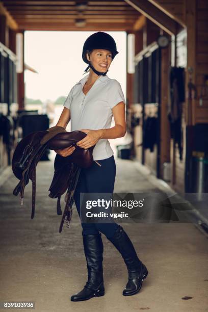 frau in einer scheune, die vorbereitung für die ausbildung - equestrian helmet stock-fotos und bilder