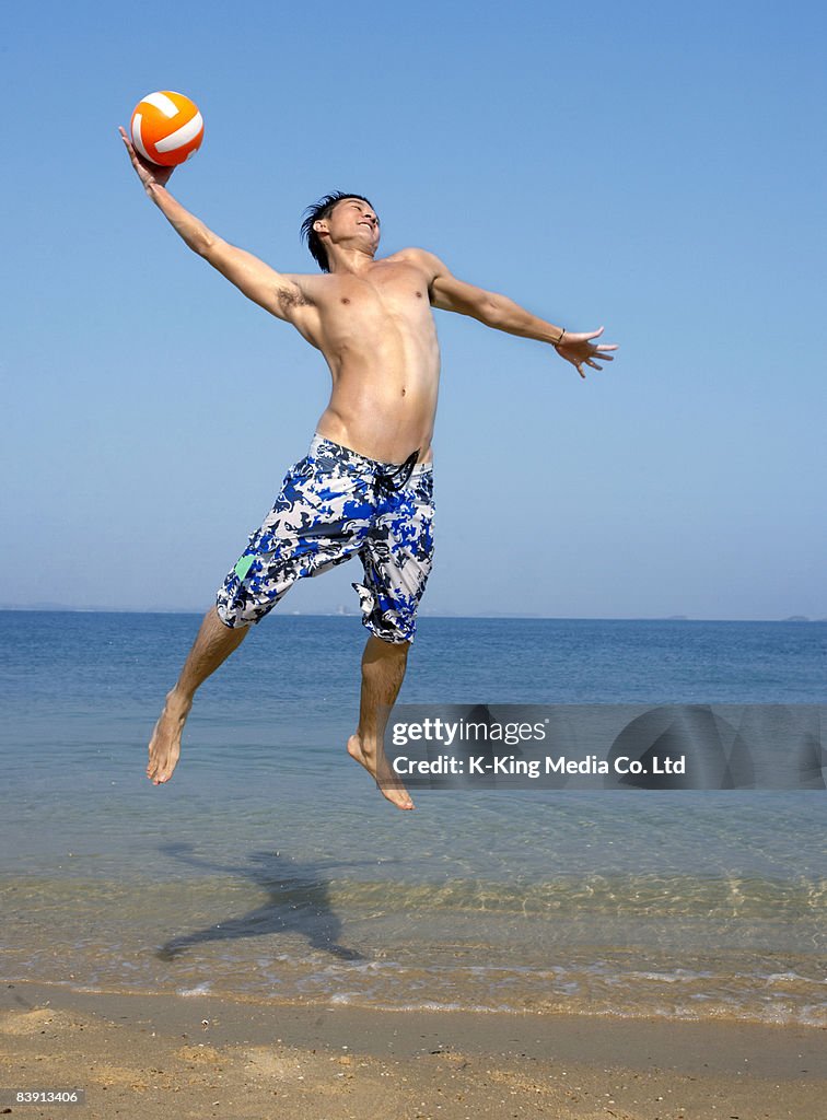 Man jumping in air with ball on beach