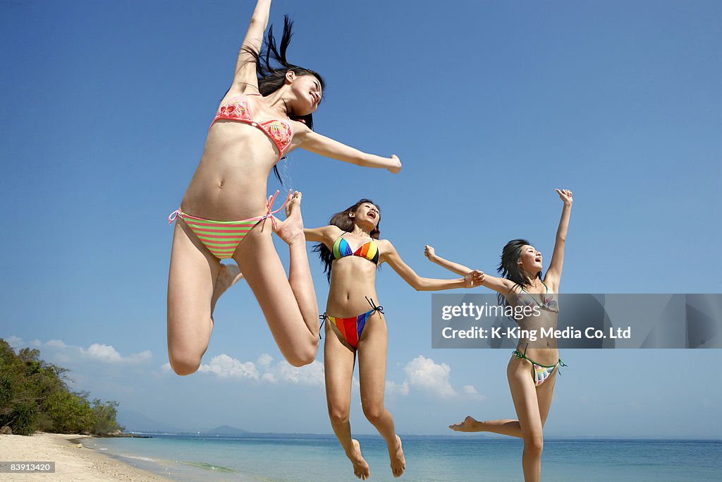 Women jumping in air on beach.