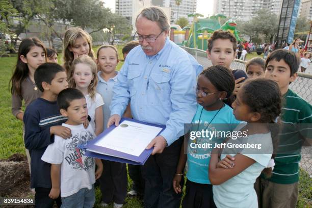 Man reading a proclamation to a group of children at the Earth Arbor Day family event for Captain Planet's Carnival.