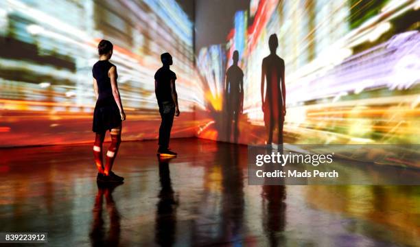 man and woman looking at abstract cityscape being projected onto the wall in a gallery space - art gallery people fotografías e imágenes de stock