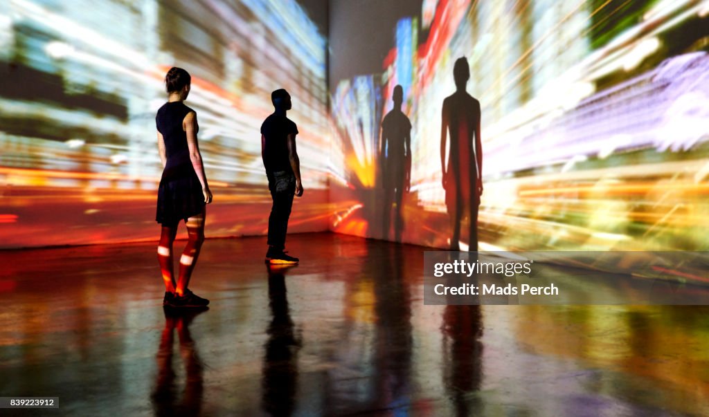 Man and woman looking at abstract cityscape being projected onto the wall in a gallery space