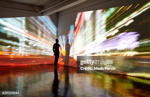 Man looking into a nighttime cityscape being projected in gallery space Man looking into a nighttime cityscape being projected in gallery space