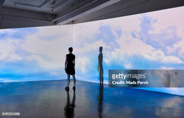 girl looking into a large scale projected image of skies - giant woman photos et images de collection