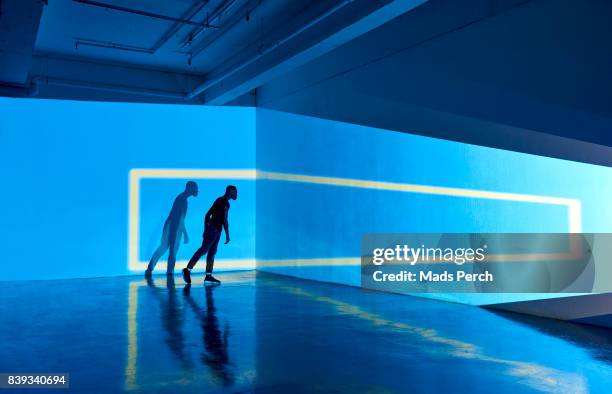 man with large scale graphic shape projected on to the wall behind him - projection mapping stockfoto's en -beelden