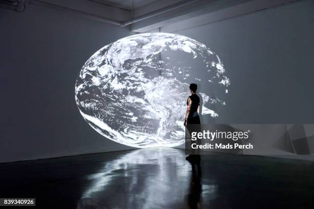 girl standing in gallery space looking at large scale projection of planet earth - one world stockfoto's en -beelden