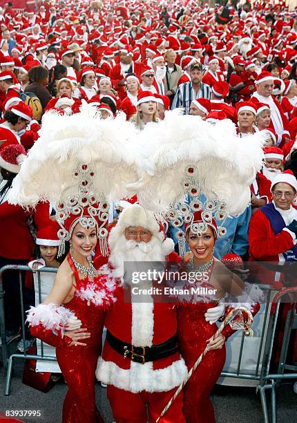 Showgirls Brooke Opheim and Heather Remillard pose with a Santa Claus actor in front of thousands of runners dressed in Santa Claus outfits before...