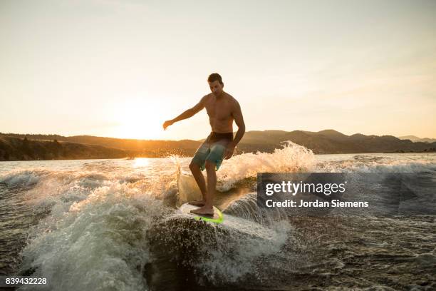 a man wake surfing behind a boat - wakeboarden stock-fotos und bilder