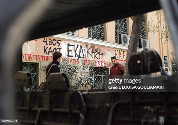 People walk by a burnt car and graffitti on a wall, reading "Revenge," in the vicinity of the occupied Athens Polytechnic University on December 8,...