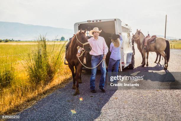 een man en een vrouw krijgen hun paarden uit een paardaanhangwagen. - paardenwagen stockfoto's en -beelden