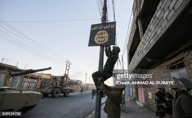 Member of Hashed Al-Shaabi removes a sign on a lamp post bearing the logo of the Islamic State group as Iraqi forces advance inside the town of Tal...