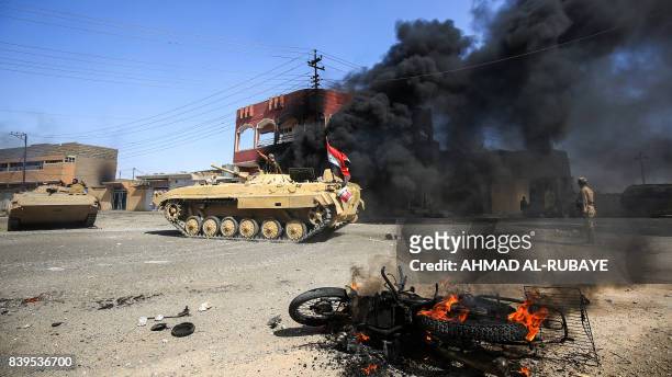 Smoke billows from a burning building and motorcycle as Iraqi forces' armoured vehicles advances through a street in the town of Tal Afar, west of...