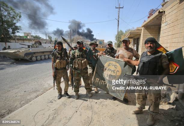Fighters of Hashed Al-Shaabi flash the victory gesture as they hold upside down a banner bearing the logo of the Islamic State group, during the...