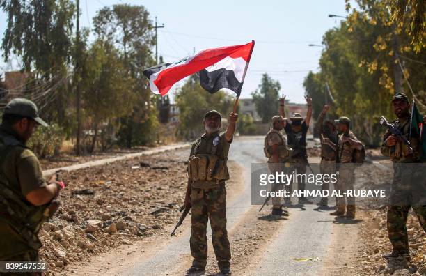 Fighter of the Hashed Al-Shaabi waves an Iraqi flag as others behind flash the victory gesture, during the advance through the town of Tal Afar, west...