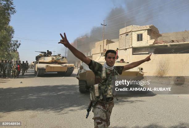 An Iraqi forces' fighter flashes the victory gesture as others, backed by the Hashed Al-Shaabi , advance through a street in the town of Tal Afar,...