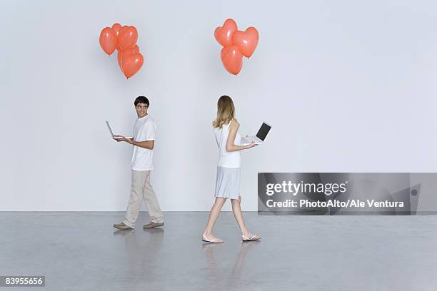 man and woman walking past each other, both carrying laptop computers and heart balloons - dating stockfoto's en -beelden