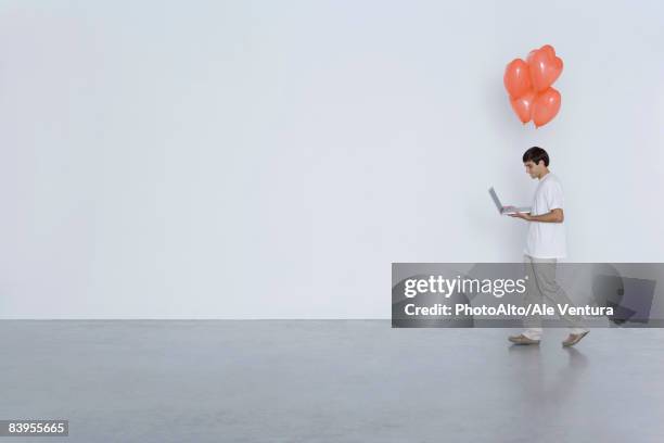 man carrying laptop computer and heart balloons, side view - vrijgezel stockfoto's en -beelden