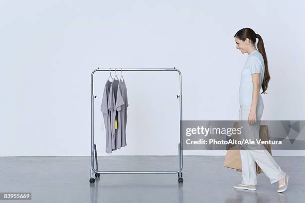 woman walking toward rack of tee-shirts, carrying shopping bags - gancho imagens e fotografias de stock