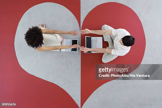 man and woman sitting with laptops on large heart, arms out, touching hands, overhead view - relation à distance photos et images de collection