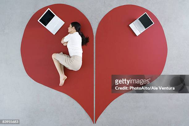 woman lying on the ground with laptop on large broken heart, abandoned laptop behind her - bent stockfoto's en -beelden