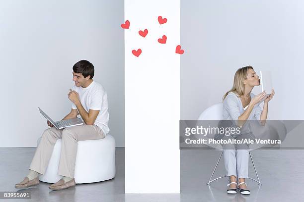 woman kissing laptop computer, man looking at his own laptop and smiling, hearts in the air between them - long distance relationship stock pictures, royalty-free photos & images