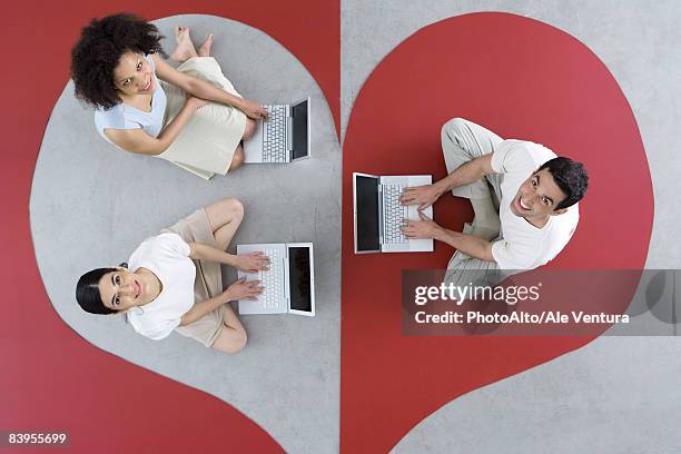two women and one man sitting on large heart, using laptop computers, smiling up at camera - asymmetry fotografías e imágenes de stock