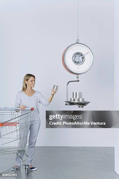 woman standing with shopping cart, placing cans on scale - inexpensive stockfoto's en -beelden