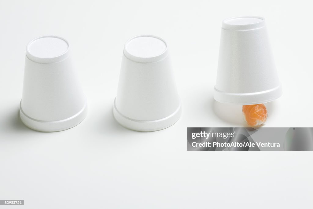 Three disposable cups in row, end cup lifted revealing single piece of nigiri sushi 