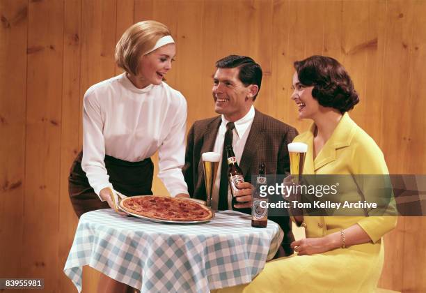 Group of two women and a man enjoy a pizza and some Ballantine beer, ca. 1950s. United States.