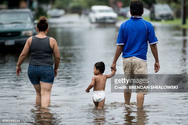 People walk through flooded streets as the effects of Hurricane Harvey are seen August 26, 2017 in Galveston, Texas. - Hurricane Harvey left a trail...