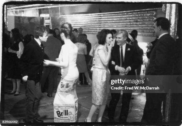At a party at the his studio, the Factory , American pop artist Andy Warhol listens as Margarette Lampkin whispers in his ear while next to them,...