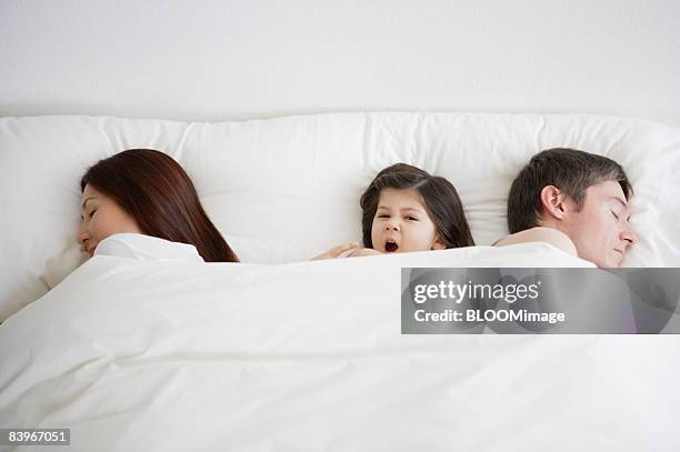 girl yawning between parents in bed - yawning mother child stock pictures, royalty-free photos & images