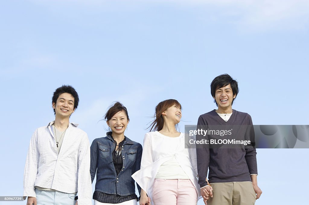 Portrait of men and women standing hand in hand against blue sky, smiling