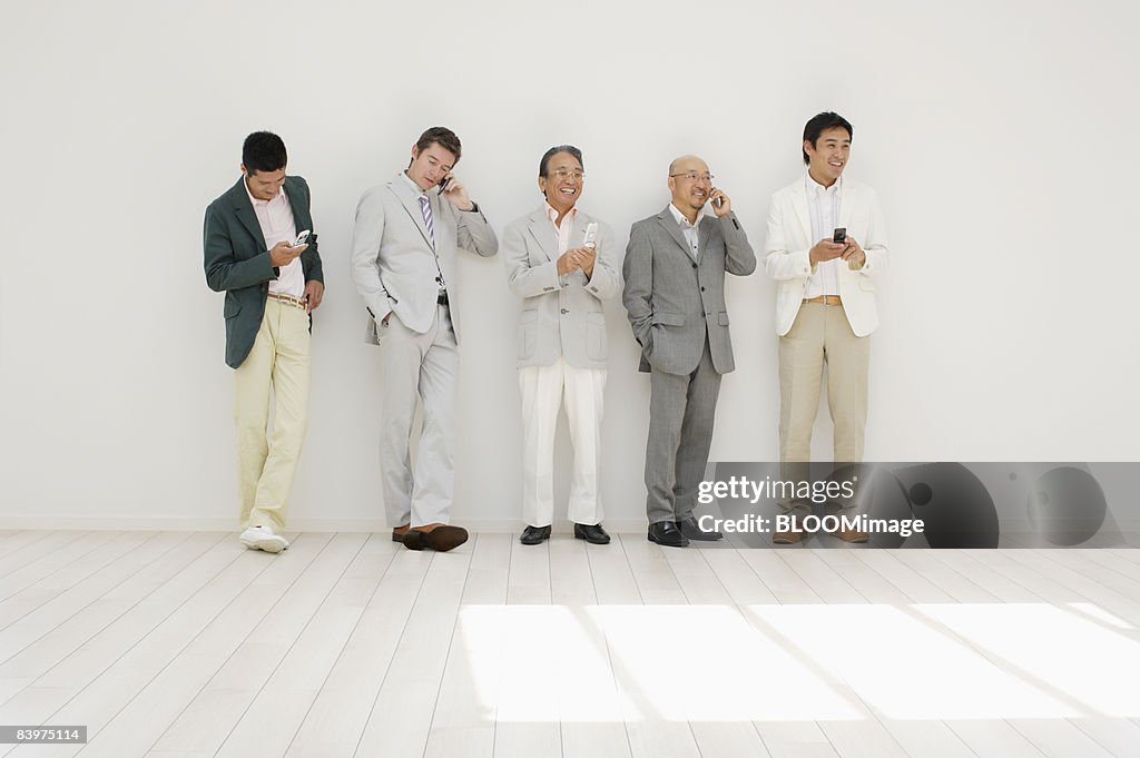 Businessmen standing in row against wall, using cellular phone