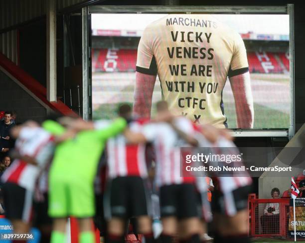 Cheltenham Town players get together whilst a message of support for Vicky Veness is shown on the big screen during the Carabao Cup Second Round...
