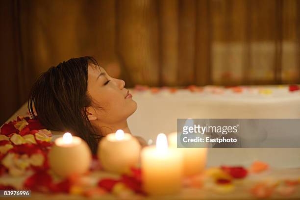 woman taking bath, with candles and flower petals. - bath spa stock-fotos und bilder