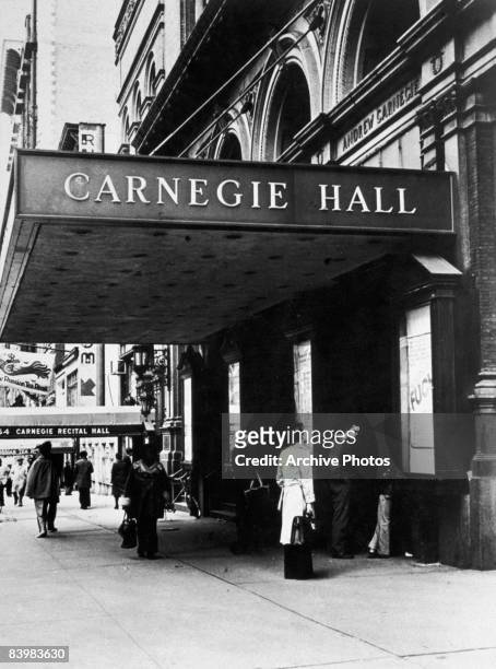 People stand outside the entrance to Carnegie Hall, midtown Manhattan, New York City, circa 1980. Violinist Joseph Fuchs is appearing there,...