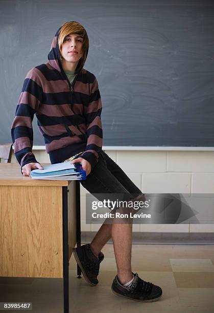 teen boy sitting on teachers desk, portrait - teen boy shorts stock-fotos und bilder